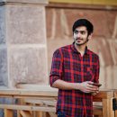 Young indian student man at red checkered shirt and jeans posed at city with mobile phone at hands.